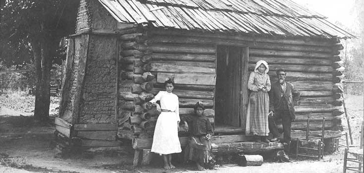 "A Croatoan Indian home, front view, with man and woman to right of door. Two young women at left," H.19XX.325.26, Image courtesy of the N.C. Museum of History.