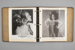 Image of a photo album with two pictures of people. The photo on the right shows the famous drag queen known as Divine wearing a large wig and a cheetah-print strapless dress. Both photos are signed.