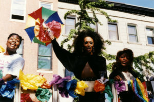 Photo of three Black women holding colorful paper flowers.