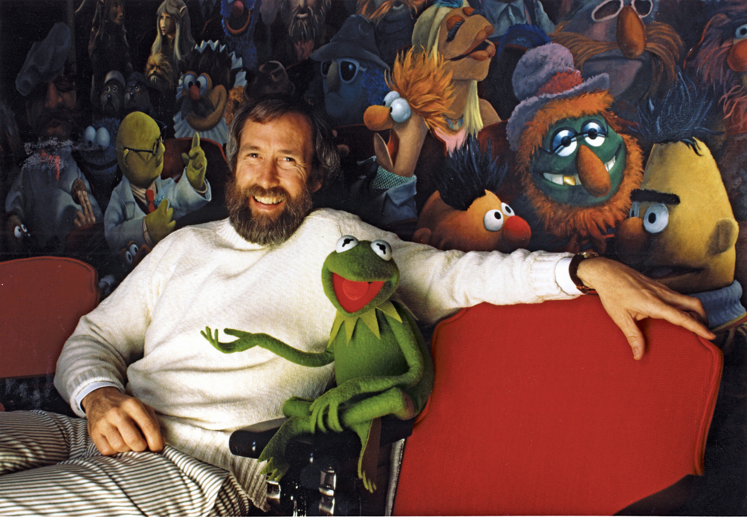 Jim Henson and his iconic creation Kermit the Frog in front of a mural of Muppets characters by Coulter Watt.