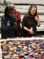 A photo of several women looking over a kaleidoscope quilt