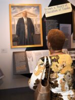 A photo of a woman looking at a painting of Thurgood Marshall