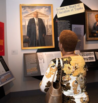 A photo of a woman looking at a painting of Thurgood Marshall