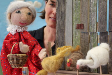 A close-up photo of a needle-felted elder woman and needle-felted chickens