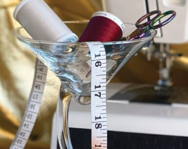 A photo of a cocktail glass with spools of thread and measuring tape