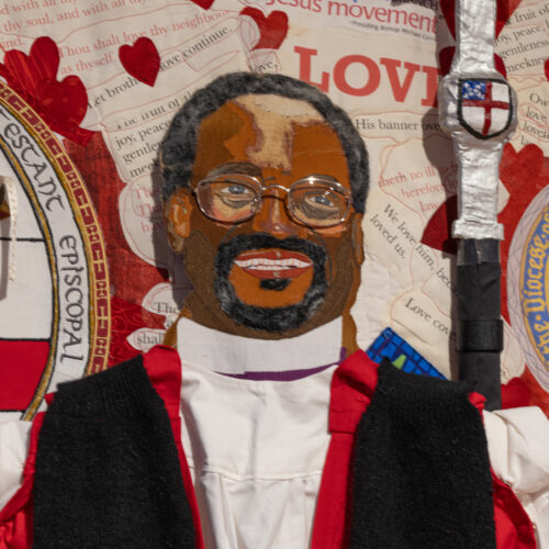 Detail of a quilted artwork featuring the portrait of a Black clergyman wearing vestments. The word love and red heart shapes surround the figure.
